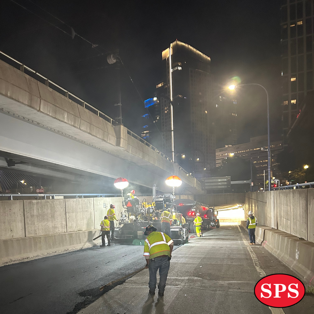 Men in safety vests watching paving happen.